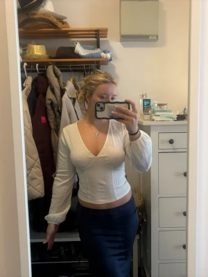 Vit ribbad croppad v-ringad topp - Snygg vit croppad topp med ribbad struktur och v-ringning. Långa ärmar med lätt puff och smal passform som framhäver figuren. Perfekt att styla med både jeans och kjol för en trendig look.