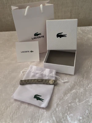 Silverfärgat armband från Lacoste - Jag erbjuder ett nytt unisex Lacoste-armband. Armbandet är justerbart och mäter cirka 21 cm i längd. Silverfärgen ser vacker ut på handleden. Det levereras med alla tillbehör som visas på bilderna. Mycket snabb och effektiv leverans. Jag rekommenderar det!