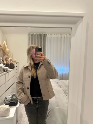 Beige kappa från Nelly - Stilren beige kappa från Nelly i storlek S. Kappan har klassisk krage, stora knappar framtill och två rejäla fickor. Materialet är mjukt och ger en lyxig känsla. 