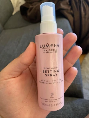 Lumene Dewy Glow Setting Spray - Fräsch face mist från Lumene i rosa plastflaska med sprayfunktion. Ger lyster och återfuktning till huden, perfekt för att fixera sminket och få en glowig finish. Innehåller 100 ml och passar alla hudtyper. Vegansk formula.