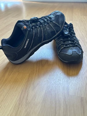 Merrell sneakers / vandringsskor stl 42 – Svart mesh med reflekterande detaljer - Säljer ett par Merrell skor i storlek 42. Lätta och bekväma skor som passar bra för promenader, lätt vandring eller vardagsbruk. Utrustade med snabbsnörning för enkel av- och påtagning samt bra grepp i sulan.  • Märke: Merrell • Storlek: 42 • Färg: Svart (Black/Wild Dove) • Snabbsnörning • Bra grepp i sulan • Använda men i okej skick  Observera: En mindre skada finns vid snörningen (se bild), men skorna fungerar fortfarande som de ska.  Hör av dig vid intresse eller frågor.
