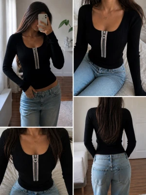 Svart ribbad topp med dragkedja - Snygg svart ribbad topp från Enzoria med lång ärm och en glittrig dragkedja framtill som har ett hjärtformat handtag. Stretchigt material som sitter tight och markerar figuren. Perfekt för dig som gillar detaljer och vill sticka ut lite extra.