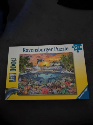 Ravensburger pussel  - Ravensburger pussel med 100 XXL-bitar, motiv av delfiner och korallrev i färgglada nyanser. Rekommenderas från 6 år och uppåt. Pusslet mäter ca 49x36 cm färdigt och levereras i en gul och vit kartong.