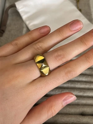 Guldfärgad ring från Edblad - Snygg guldfärgad ring från Edblad med en bred design och två pyramidformade detaljer på ovansidan. Ringen har en blank finish och känns både modern och edgy. Perfekt accessoar för att lyfta din stil.