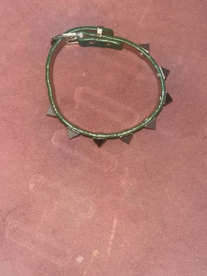 Grönt läderarmband med nitar - Snyggt grönt armband i läder med silvriga pyramidformade nitar. Perfekt accessoar för att ge din outfit en edgy touch. Justerbart spänne i metall för enkel passform.