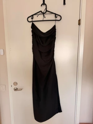 Svart långklänning med drapering - Elegant svart långklänning med smala axelband och snygg drapering framtill. Klänningen har en figurnära passform och är mer ”flowy” vid benen! Prislapp finns kvar!