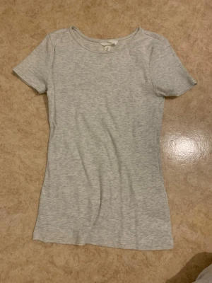 Ljusgrå ribbad t-shirt - En enkel och stilren ljusgrå t-shirt med ribbad struktur. T-shirten har rund halsringning och korta ärmar. Perfekt basplagg som passar till allt och är gjord i mjuk bomull för skön känsla.