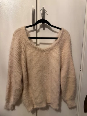 Ljus rosa fluffig stickad tröja - Mysig ljus rosa stickad tröja med fluffig textur och bred v-ringning. Tröjan har långa ärmar och en avslappnad passform. Baksidan har en snygg rynkning som ger extra detalj. Perfekt för dig som gillar en trendig och bekväm stil.