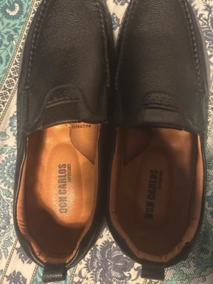 Svarta loafers från Don Carlos - Säljer ett par svarta loafers från Don Carlos i äkta läder. Skorna har en klassisk design med rundad tå, diskreta sömmar och bekväm innersula i brunt skinn. Perfekta för dig som gillar stilrena och tidlösa skor.