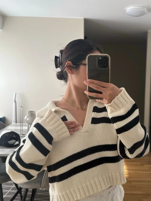 Randig stickad tröja svart vit - Snygg stickad tröja i offwhite med svarta breda ränder och krage. Tröjan har en avslappnad passform, långa ärmar och ribbade muddar. Perfekt för en trendig och avslappnad look.
