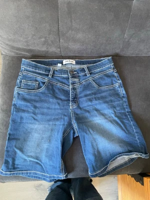 Blå jeansshorts från John Baner - Snygga blå jeansshorts från John Baner med klassisk femficksdesign och kontrastsömmar. Shortsen har normal passform, bälteshällor och knappgylf. Perfekta för varma dagar och enkla att matcha med olika stilar. Skriv vi funderingar💕