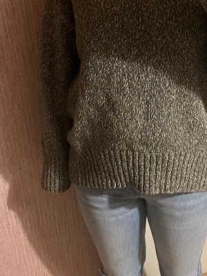 Olivgrön melerad stickad tröja - Stickad tröja i olivgrönt melerat. Tröjan har en avslappnad oversized passform och är långärmad, Materialet känns mjukt och tjockt, vilket gör den extra mysig.