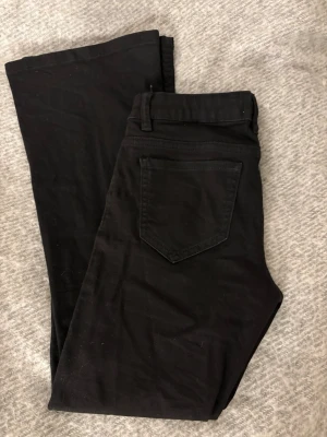 Svarta jeans från Lindex (Freja) - Svarta jeans från Lindex modell Freja med klassisk femficksdesign och utsvängda. Jeansen har hällor för bälte och är tillverkade i ett mjukt bomullsmaterial med lite stretch för extra komfort. Grenhöjd: 20 cm