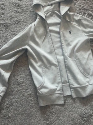 Ljusgrå hoodie från Polo Ralph Lauren - Säljer en fräsch polo zip hoodie i nästan ny skick. Använd i några tillfällen.  Storlek Xs Pris: 650kr Skriv vid funderingar.