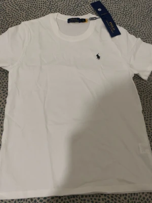 Vit t-shirt från Polo Ralph Lauren - Klassisk vit t-shirt från Polo Ralph Lauren med rund halsringning och den ikoniska broderade loggan på bröstet. Tillverkad i mjuk bomull för en skön känsla och enkel stil. Perfekt basplagg för alla tillfällen.