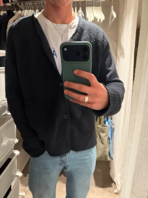 Mörkblå stickad kofta med knappar - Mörkblå stickad kofta med v-ringning och tre knappar framtill. Koftan har långa ärmar och en avslappnad passform, perfekt att slänga över en t-shirt. 