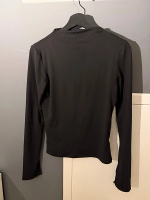 Svart långärmad polotröja - En enkel och stilren svart långärmad polotröja i mjukt och stretchigt material. Tröjan har en smal passform och hög krage, perfekt att matcha med olika outfits. Passar dig som gillar minimalistisk och clean stil.