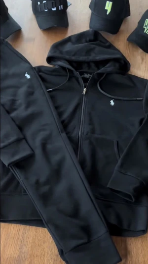 Svart hoodie från Polo Ralph Lauren - Snygg svart hoodie från Polo Ralph Lauren med dragkedja framtill och klassisk huva. Ikoniska lilla vita loggan broderad på bröstet. Tillverkad i mjukt och bekvämt material, perfekt för en avslappnad och stilren look.