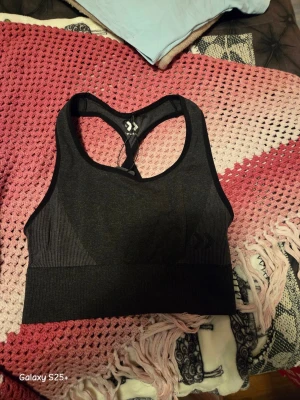 Svart sport-bh från Dcore - Snygg svart sport-bh från Dcore med brottarrygg och diskret logga framtill. Tillverkad i stretchigt material som ger bra stöd vid träning. Perfekt för gymmet eller löprundan.