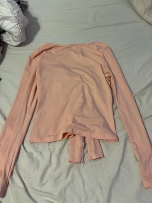 Ljusrosa omlottopp med knyt - Trendig ljusrosa omlottopp med långa ärmar och knyt framtill. Tillverkad i mjuk bomull som känns skön mot huden. Perfekt för dig som vill ha en enkel men snygg topp med lite extra detalj framtill.