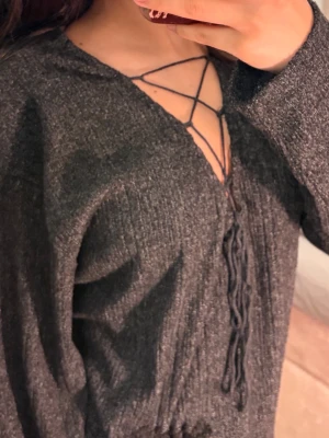 Mörkgrå stickad tröja med snörning🌸 - Säljer en mörkgrå stickad tröja med trendig snörning framtill och långa ärmar. Tröjan har en avslappnad passform och ribbad struktur som ger en cool vibe. Perfekt för dig som gillar en unik detalj i garderoben.