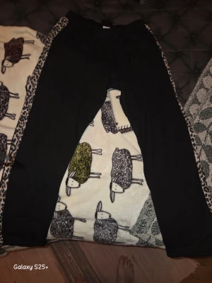 Svarta mjukisbyxor med leoparddetaljer - Säljer ett par svarta mjukisbyxor med leopardmönstrade detaljer längs sidorna. Byxorna har avslappnad passform och resår i midjan. Perfekta för chill dagar eller när du vill ha en cool och bekväm look.