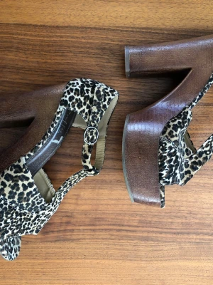 Leopardmönstrade platåsandaler Duffy - Säljer ett par sandaler från Duffy med leopardmönster. Skorna har hög platåklack i trälook och justerbart spänne vid ankeln. Ovandelen är i textil med djurmönster som sticker ut. Perfekta för dig som vill ha en statement-look.