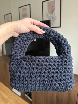 Mörkblå handvirkad handväska - Unik handväska i mörkblått, handvirkad med tjockt garn för en chunky och trendig look. Väskan har en mjuk, rektangulär form med integrerat handtag och passar perfekt för dig som gillar personliga accessoarer. Materialet är troligtvis bomullsgarn.