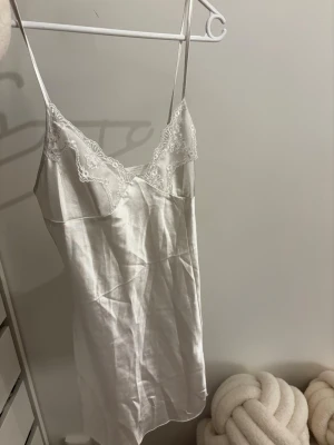 Vitt satinnattlinne med spetsdetaljer - Säljer ett elegant vitt nattlinne i satin med tunna axelband och fina spetsdetaljer vid bysten. Nattlinnet har en mjuk och glansig yta som känns lyxig mot huden. Använd vid 2 tillfällen, tvättad. Fått i present oklart varifrån den är köpt. 