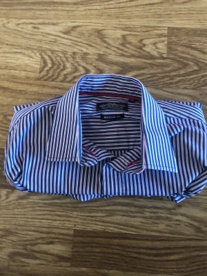 Blårandig skjorta från Hampton republik  - Klassisk blårandig skjorta från Hampton republik med regular fit. Skjortan har långa ärmar, knappar framtill och en snygg krage. Tillverkad i bomull för en skön känsla och stilren look. Perfekt för dig som gillar tidlös design och vill ha något som funkar till det mesta.