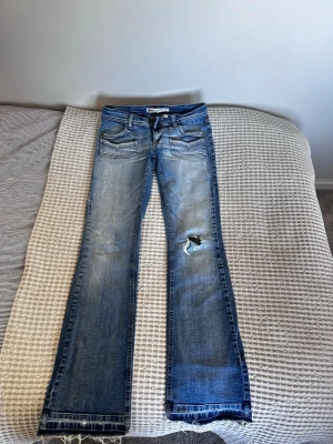 Blå bootcut jeans från ONLY - Säljer ett par ljusblå bootcut jeans från ONLY med slitningar och hål på ena knät. Är i storlek 40, men skulle säga att de passar 36/38! Jeansen har fem fickor, låg midja och råa kanter nertill. Klassisk denimlook med snygga detaljer och kontrastsömmar.❣️