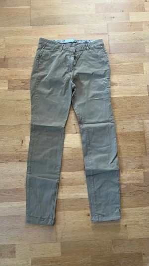 Gröna chinos - Snygga gröna chinos med smal passform och klassiska fickor fram och bak. Byxorna har bälteshällor och uppvikta benslut för en avslappnad look. Perfekta till en stilren outfit och tillverkade i mjukt bomullstyg.