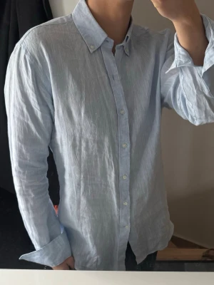 Ljusblå linneskjorta från John Henric - Säljer en stilren ljusblå skjorta från John Henric i 100% linne. Skjortan har klassisk krage med knappar, lång ärm och knappstängning framtill. Perfekt för en clean och avslappnad look.