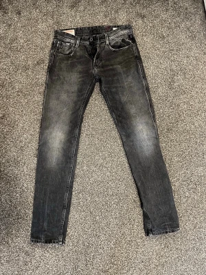 Svarta Replay anbass i slim fit jeans med slitningar - Säljer ett par svarta slim fit jeans med snygga slitningar och tvättade detaljer. Jeansen har klassisk femficksmodell och normal midja. Perfekta för dig som gillar en modern och avslappnad stil.