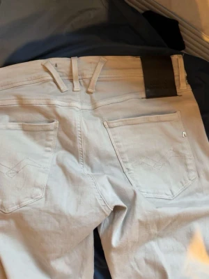 Ljusgrå jeans från Replay - Säljer ett par ljusgrå jeans från Replay med klassisk femficksdesign och snygga sömdetaljer på bakfickorna. Jeansen har en rak passform och är tillverkade i en mjuk bomullsblandning med lite stretch för extra komfort.