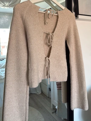 Beige stickad cardigan med knytband - Jättefin stickad tröja med öppen rygg, har små glitter i sig. Den är helt oanvänd. Gina tricot xs 14+