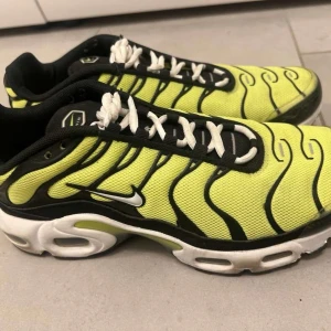 Nike Air Max Plus gul/svart sneakers - Nike Air Max Plus sneakers i neon-gult mesh med svarta och vita detaljer. Skorna har den ikoniska vågdesignen, vit sula med synliga Air-enheter och svart swoosh på sidan. Klassisk snörning och låg profil. Perfekta för dig som gillar streetwear och vill sticka ut.