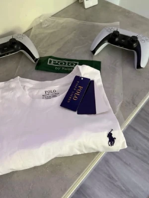 Vit t-shirt från Polo Ralph Lauren - Klassisk vit t-shirt från Polo Ralph Lauren med den ikoniska broderade loggan i marinblått på bröstet. Tillverkad i mjuk bomull och har en normal passform. Perfekt basplagg för en clean och stilren look.