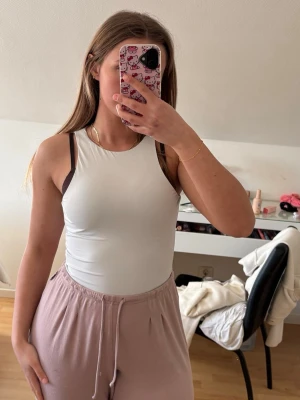 Vit ärmlös body - Säljer en enkel och stilren vit l bodt med rund halsringning. Toppen är tight i passformen och ärmlös, perfekt för varma dagar eller som lager under en skjorta. Materialet känns mjukt och stretchigt, vilket gör den bekväm att bära hela dagen. Aldrig använd!