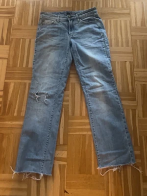 Ljusblå raka jeans med slitningar - LITEN I STORLEKEN!!! Ljusblå jeans med rak passform och råa, fransiga benslut. Snygga slitningar på ena benet och broderade detaljer på bakfickorna. 