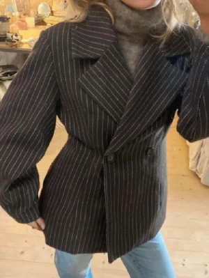 Randig oversized kavaj  - Säljer en svart kavaj med vita tunna ränder i oversized modell. Dubbelknäppt framtill med breda slag och markerade axlar. 