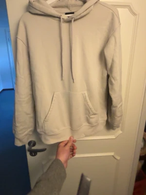 Beige hoodie från H&M med huva - Säljer en stilren beige hoodie från H&M med klassisk känguruficka och justerbar huva med dragsko. Hoodien har en avslappnad passform och är tillverkad i mjukt bomullsmaterial. Perfekt för en chill och enkel look.