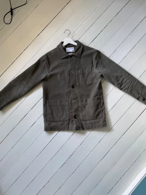 Grön overshirt från Selected Homme - Stilren grön overshirt från Selected Homme i mjuk manchester. Klassisk rak passform med tre fickor framtill och knäppning med stora knappar. Perfekt lager på lager-plagg med krage och diskret struktur i tyget. Storlek S men kan lika gärna passa M.