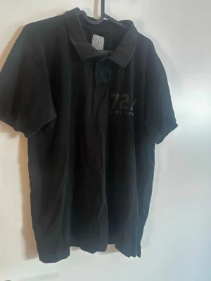 Svart pikétröja med tryck - Klassisk svart pikétröja med krage och knappar framtill. Tryck med siffran 72 och texten 'CTRL SPORT' på bröstet. Perfekt till en avslappnad stil och enkel att matcha med jeans eller shorts. Rök och djurfritt hem. Pruta gärna!🌸