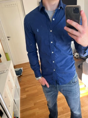 Marinblå skjorta från Polo Ralph Lauren - Snygg marinblå skjorta från Polo Ralph Lauren med klassisk krage och vita knappar. Slim fit-modell i mjuk bomull, perfekt för en clean och stilren look. Passar till allting och perfa för varmare tider.                                                        Snabb frakt 📦 Messa vid minsta fundering!! 💬 