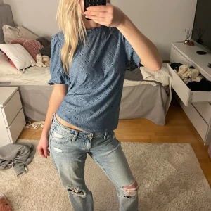 Blå broderad blus med puffärm - Säljer en blå blus med broderade detaljer och korta puffärmar. Toppen har en avslappnad passform och rund halsringning. Perfekt för dig som gillar en söt och trendig stil.