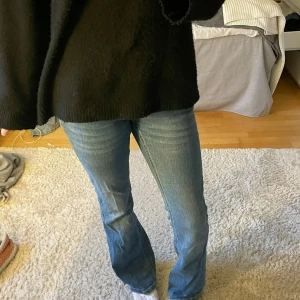 Blå bootcut jeans - Säljer ett par blå bootcut jeans med mellantvätt och klassiska fem fickor. Jeansen har en lätt utsvängd passform nedtill och synliga sömmar. Perfekta för en avslappnad och trendig look. Materialet är denim i bomull.