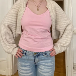 Beige croppad stickad bolero - Säljer en beige croppad stickad bolero med långärmad och oversized passform. Perfekt att slänga över ett linne eller t-shirt för en chill och trendig look. Mjuk och skön med breda ärmar och ribbad struktur.