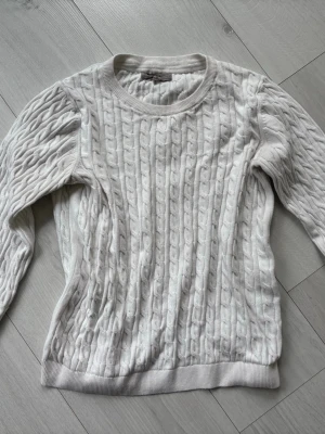 Vit kabelstickad tröja H&M - Kabelstickad tröja i mjuk vit bomullsblandning från H&M. Klassisk rund halsringning, ribbade muddar vid ärmslut och nederkant. Snygg och enkel design som passar till allt. Perfekt för lager på lager under kyliga dagar. Aldrig använd!