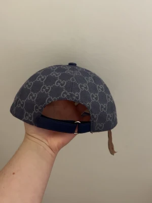 Blå GG-mönstrad keps från Gucci - Säljer en blå keps från Gucci med det klassiska GG-monogrammet över hela kepsen. Kepsen har böjd skärm, justerbart band bak och är tillverkad i ett slitstarkt tygmaterial. Perfekt för dig som vill ha en stilren och lyxig accessoar.